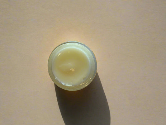 A small jar of eye cream on a plain background, viewed from above.