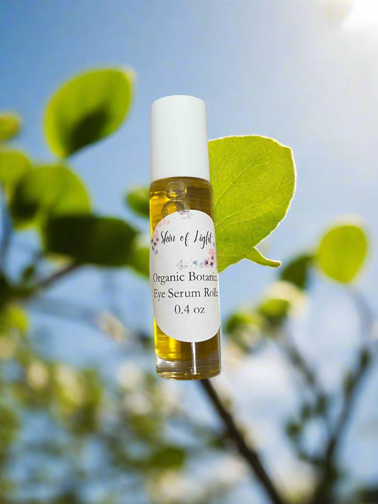 A bottle of organic eye roller serum with a white dropper, labeled 'Skin of Light Organic Botanical Eye Roller', placed on a leaf against a sunlit background.