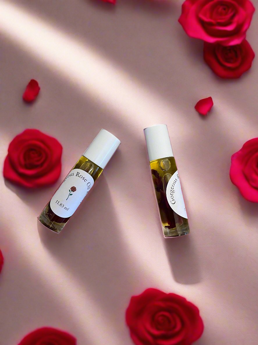 Two small roller bottles of rose oil placed on a surface with a few red rose petals scattered around, the bottles have white labels and are filled with a yellow liquid.