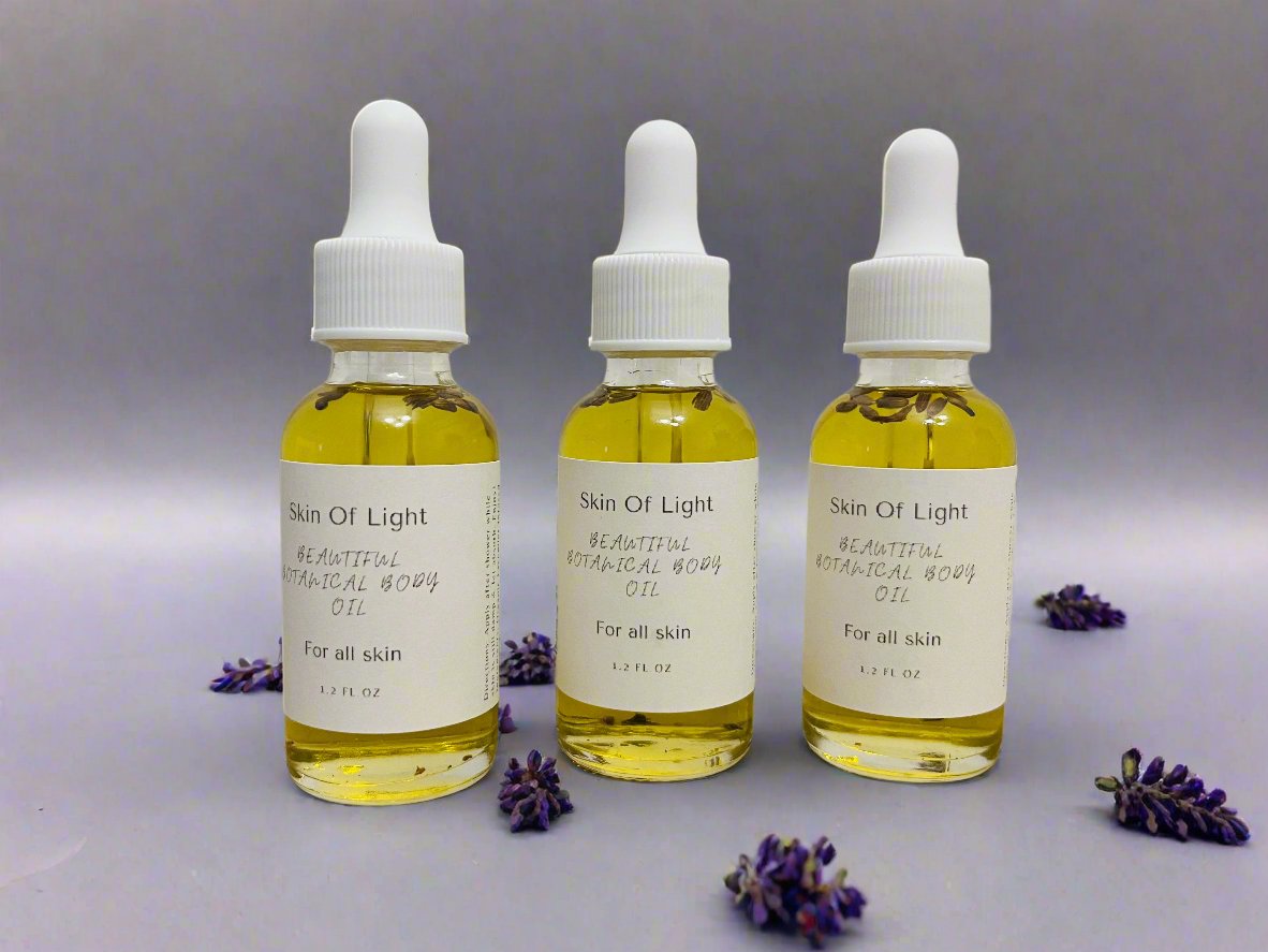 Three travel-sized bottles of body oil with dropper caps, labeled 'Skin of Light', positioned against a light grey background with purple flowers scattered around.