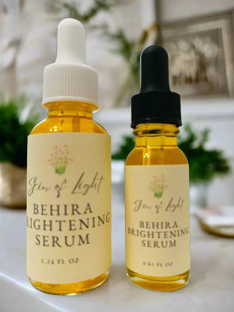 Two glass bottles with dropper caps labeled 'Skin of Light BEHIRA BRIGHTENING SERUM', one with a white cap and the other with a black cap.