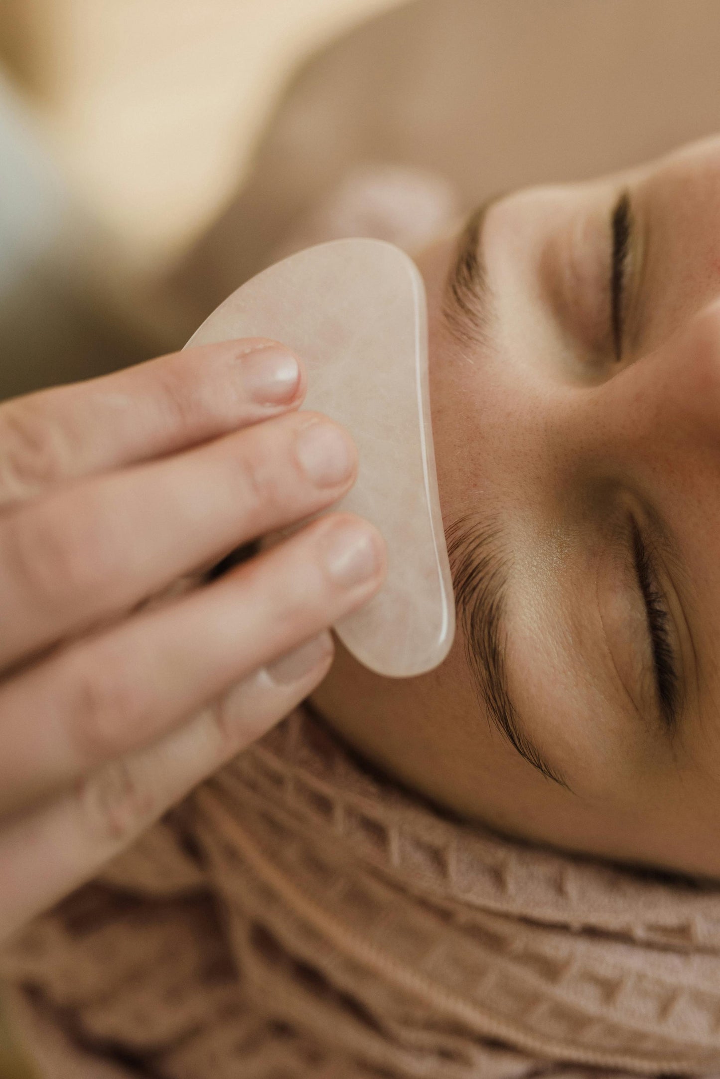 Person using a gua sha tool on their face with a blurred background