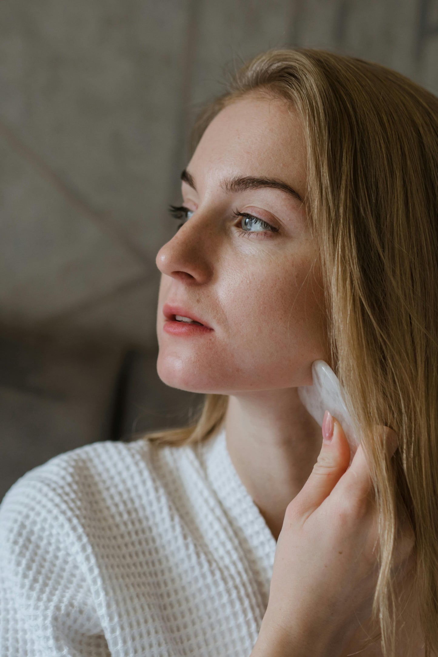 Woman applying skincare product to her face with gua sha