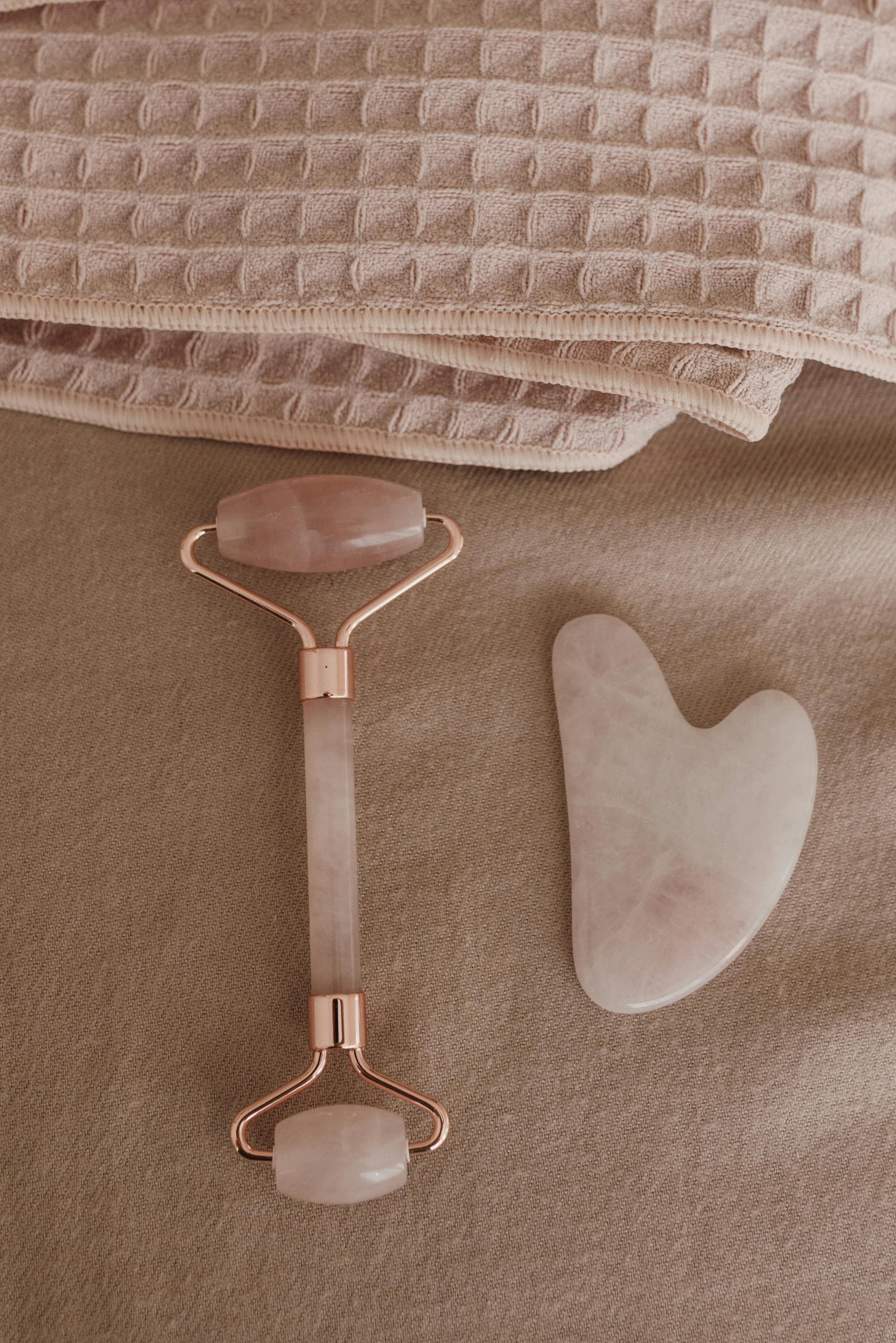 Gua Sha tool and roller on a textured beige surface